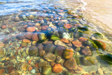 Clear sea water. Small stones at the bottom near the shore. Texture transparent clear water