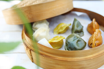 Traditional Chinese dumplings in a bamboo steamer basket. Colorful dim sum cooked on steam, selective focus.