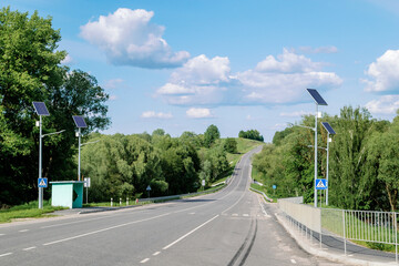 Fototapeta na wymiar Lamp post with solar panel system on road with blue sky and trees. Autonomous street lighting using solar panels. Street lamp, on batteries from the sun. Alternative renewable energy systems.