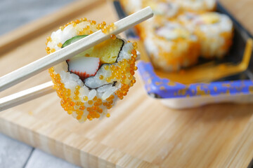 chop stick holding Sushi roll with salmon, shrimps and avocado 