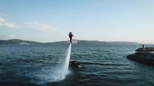 Show over the water on a flyboard. A woman in a red dress plays the saxophone, a man flies with her together.