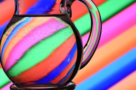 Ilusi&oacute;n &oacute;ptica creada mediante la refracci&oacute;n de la luz con un recipiente de crital lleno  de agua y lineas diagonales de colores	