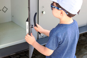 kid try to lock metal cabinet for keeping things.gray metal door with key.organizer for bags shoes clothes,steel locker for office gym market school or bank.numbers engraved on doors.back view closeup