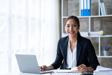 Beautiful smiling Asian businesswoman working with laptop while sitting at table
