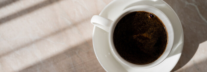 top view of cup of black coffee and white saucer on marble surface, banner.