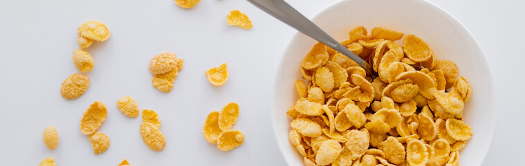 top view of bowl with crispy corn flakes and spoon isolated on white, banner.