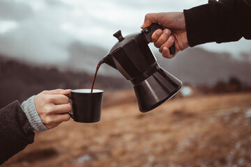 Person pouring out coffee from moka pot into cup outdoors with fog background