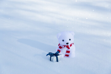 Lonely polar bear toy with a striped scarf and a gift in the snow