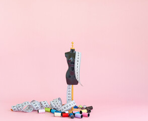 A scaled-down mannequin on a pink background with a tape for measuring and multicolored threads in...