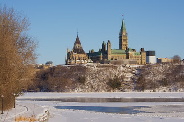 Obraz premium Gothic revival buildings and towers of parliament hill, seen from the park along Ottawa river on a sunny witer day with clear blue sky. Ontario, Canada 