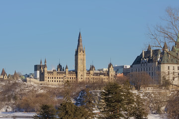 Obraz premium Gothic revival buildings and towers of parliament hill, seen from the park along Ottawa river on a sunny witer day with clear blue sky. Ontario, Canada 