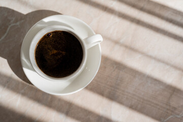 top view of cup of black coffee and white saucer on marble surface.