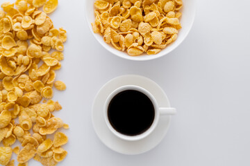 top view of bowl with corn flakes near cup of black coffee isolated on white.