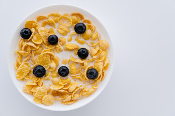 top view of crispy corn flakes in bowl with organic milk and blueberries isolated on white.