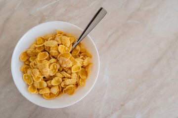 top view of bowl with corn flakes and spoon on marble surface.