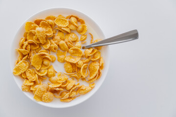 top view of crispy corn flakes in bowl with spoon and milk isolated on white.