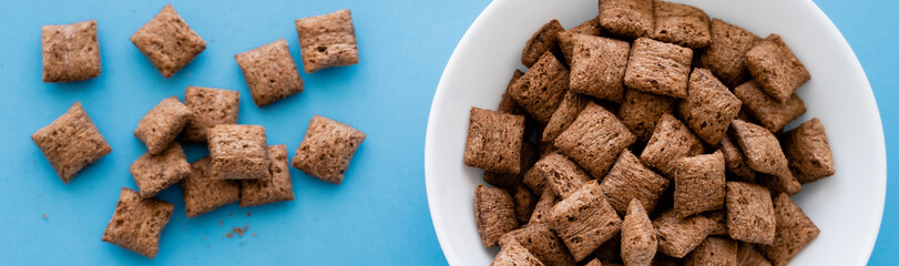 top view of chocolate cereal puffs and white bowl isolated on blue, banner.