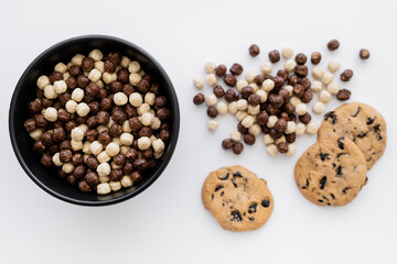 top view of cereal balls in bowl near chocolate chip cookies isolated on white.