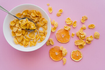 top view of dried oranges near bowl with corn flakes and organic milk on pink.