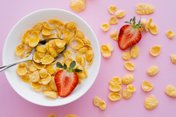 top view of bowl with corn flakes and organic strawberry on pink background.