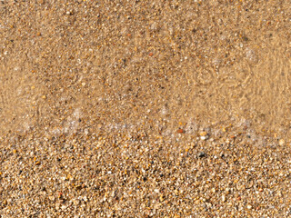 Sand texture on a bathing beach. Clear transparent water with air bubbles is visible. Top down view with fine small stones. Abstract background in the nature. Yellow bright color of the ground.