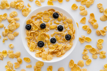 top view of tasty corn flakes in bowl with organic milk and fresh blueberries isolated on white.