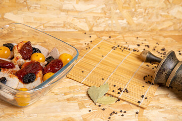 Glass baking tray with meat, cherry tomatoes, prunes and dried tomatoes. Preparation of semi-finished products and blanks in the home village kitchen. Copy space