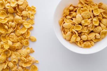 top view of dry and crispy corn flakes near bowl isolated on white.