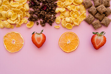 top view of assorted breakfast cereal corn flakes and crispy granola near fruits isolated on pink.