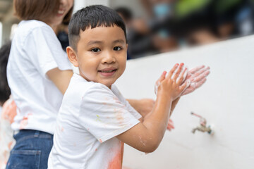 Asian boy washing hands with soap on outdoor wash basin after painting color by using his hands at school.Kids hygiene and health concept.