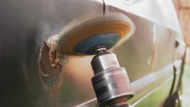 A round metal brush in the hands of a man cleans rust from a car fender. Medium plan.