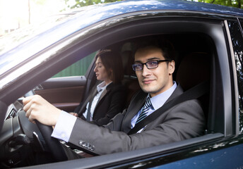 Handsome and confident businessman in black suit and his female colleague driving in luxury car	