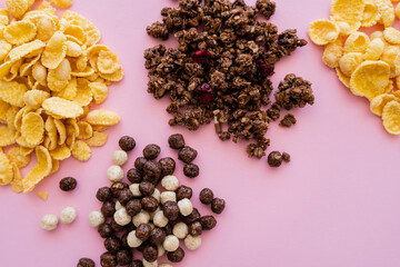 top view of corn flakes near cereal balls with vanilla and chocolate flavors and tasty granola isolated on pink.