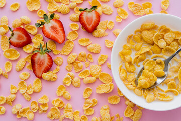 close up view of fresh sliced strawberries around crispy corn flakes and bowl on pink.