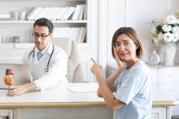 Portrait of young scared and irritated female patient and doctor cardiologist working in office of modern clinic