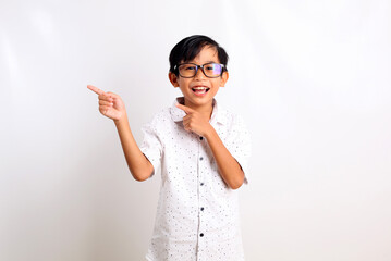 Happy asian schoolboy standing while pointing something on empty space. Isolated on white background