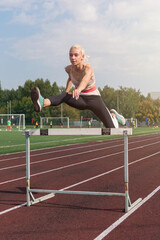 Obraz premium Young woman athlete runnner running hurdles at the stadium outdoors