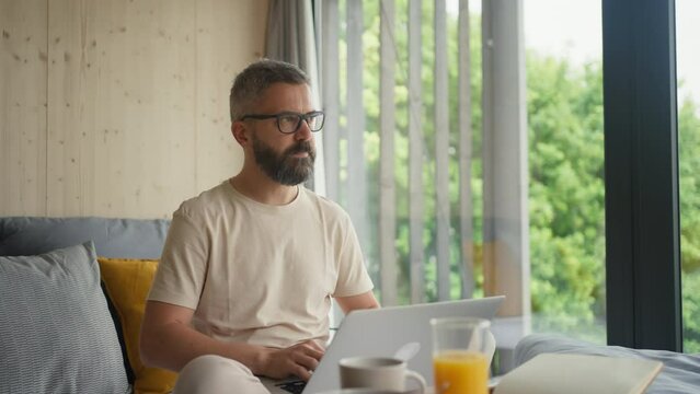 Man working on laptop in bed, while having breakfast.