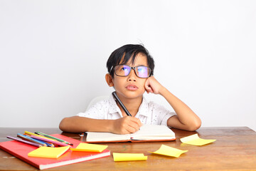 Asian schoolboy studying, doing his homework and thinking on the desk. Isolated on white background