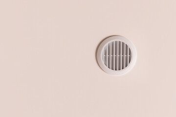 Round air vent with white plastic grate on beige ceiling