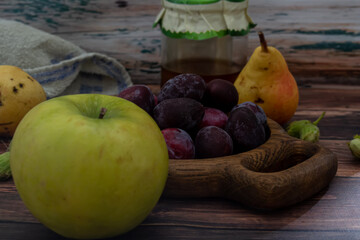 Wooden plate with fresh blue plums, apples and pears on a wooden background.