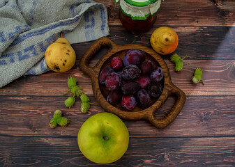 Wooden plate with fresh blue plums, apples and pears on a wooden background.
