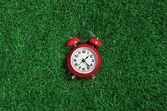 red alarm clock on green turf grass background. half past one o'clock. copy space, game time management concept. opening or closing hours. Ecological sustainable business banner