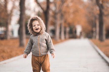 Cute baby girl 1-2 year old wearig casual stylish cloth walk in autumn park with fallen leaves outdoor. Childhood.