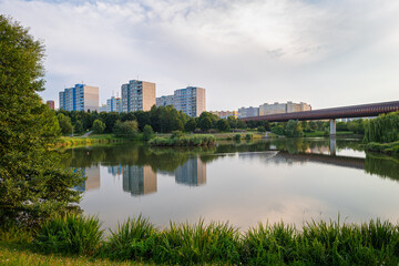 Fototapeta na wymiar Small lake in a city park and high-rise apartment buildings in suburban area Lužiny in the city of Prague