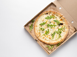 Pizza quattro formaggi (four cheese pizza) served with rocket salad leaves in cardboard box. Traditional italian dish. Top view. White background. Take away or delivery concept.