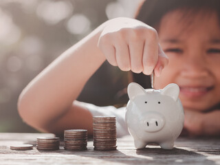 Concept of Saving Money. Happy Asian child girl save money putting coin into piggy bank, coins...