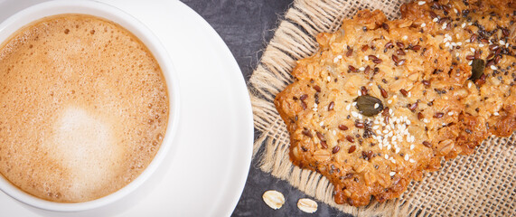 Cup of white coffee and fresh oatmeal cookies with honey and healthy seeds. Delicious crunchy...