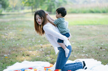Adorable little Asian boy piggyback ride with his mother while playing in summer park together....