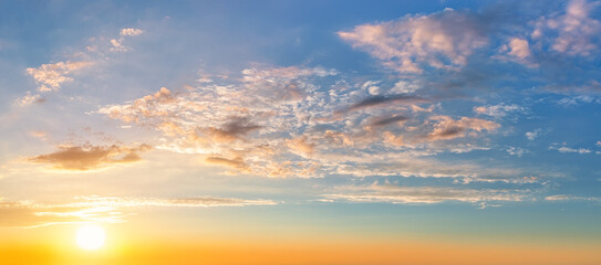 Fototapeta premium Settind sun low in the yellow blue evening sky. Light translucent orange clouds in the sunset heaven. Picturesque calm sundown skyscape. Idyllic vanilla sky wide panorama. Weather forecast.